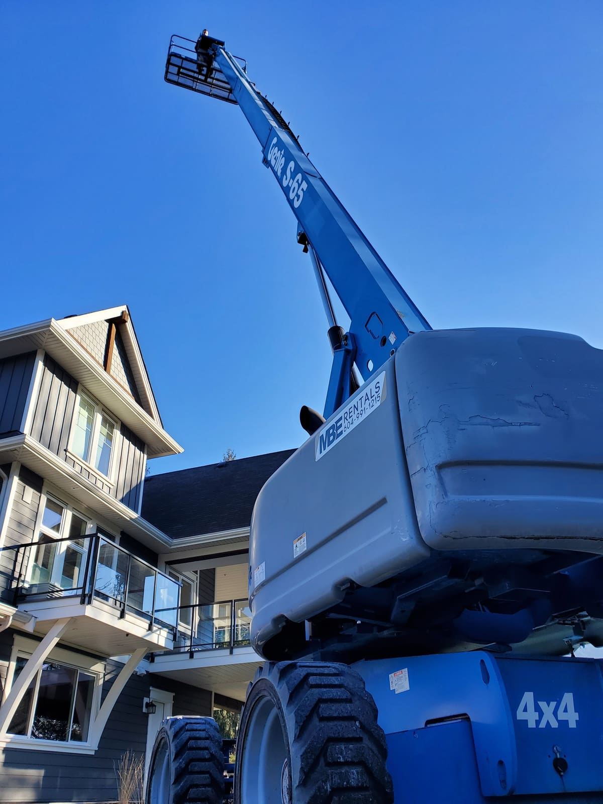 MBE Rentals Genie S-65 boom lift reaching over a rooftop in Rosedale, BC